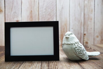Empty frame and bird statue on wooden background