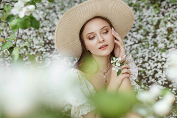 An attractive long-haired woman walks in the spring in the park of blooming apple trees.