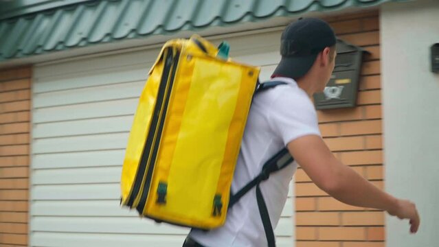 Young fast delivery boy riding bike walking to gate ringing in door bell. Portrait of professional Caucasian courier delivering order in town. Service and speed concept
