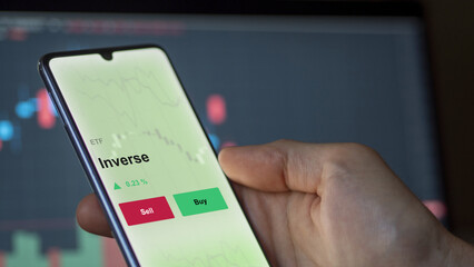 An investor's analyzing the inverse etf fund on a screen. A phone shows the prices of Inverse