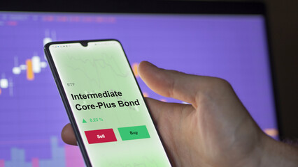 An investor's analyzing the intermediate core-plus bond etf fund on a screen. A phone shows the prices of intermediate-term ETF.