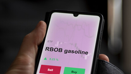 An investor's analyzing the rbob gasoline etf fund on a screen. A phone shows the prices of RBOB gasoline
