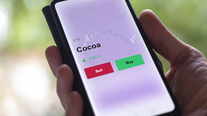 An investor's analyzing the cocoa etf fund on a screen. A phone shows the prices of cacao traded ETF.