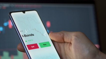 An investor's analyzing the i-bonds etf fund on a screen. A phone shows the prices of I-Bonds inflation-protected bond