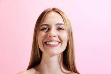 Closeup face of young beautiful girl, student looking at camera isolated on pink background. Concept of beauty, art, fashion, human emotions