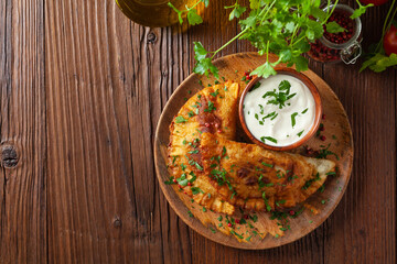 Traditional cheebureki, served on a wooden plate with sauce.