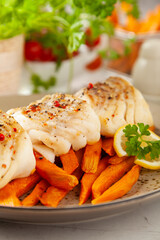 Fried pieces of cod loin, served with sweet potato fries. Light stone background.