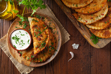 Traditional cheebureki, served on a wooden plate with sauce.