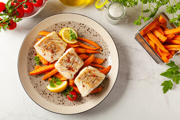 Fried pieces of cod loin, served with sweet potato fries. Light stone background.