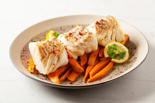 Fried pieces of cod loin, served with sweet potato fries. Light stone background.