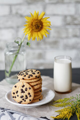 Сookies americano on a plate and a glass of fresh milk, a sunflower in a jar on the table with bricks on the background
