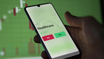 An investor's analyzing the healthcare etf fund on a screen to invest. A phone shows the prices of health care blue chips ETF.