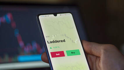 An investor's analyzing the laddered etf fund on a screen to invest. A phone shows the prices of staging and sequencing ETF