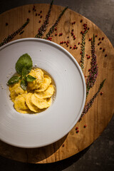 Round plate with ravioli and with cheese on top decorated with peppermint leaves and heather flowers. Black stone table. 