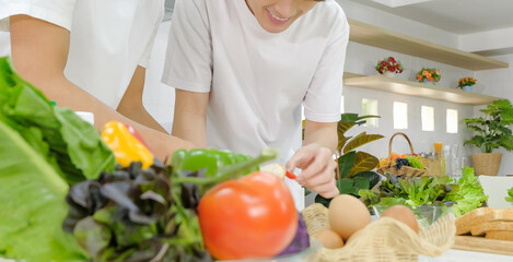 Young asian male LGBT couple happy spending time together during cooking bread salad in the kitchen with smiling face. Half portrait background. Selective focus.