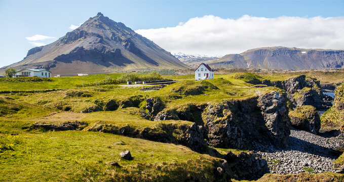 Panoramic view on Impressive Icelandic landscape. Alone  house in fishing village Arnarstapi in Iceland. Tipical Sunny Scenery with basalt rocks formation on coastline. Snaefellsnes peninsula, Iceland