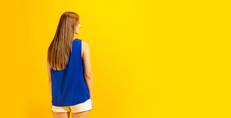 Back view of young girl with long glossy light hair isolated on bright yellow background. Concept...