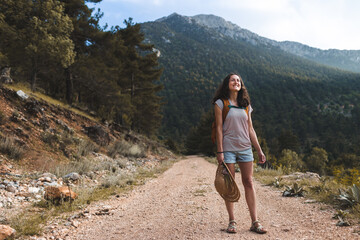 Naklejka premium A girl with a backpack and a straw hat walks along a mountain path
