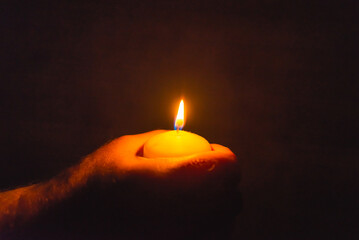 Burning candle in a mans hand religion concept.Candle in hands on a dark background.