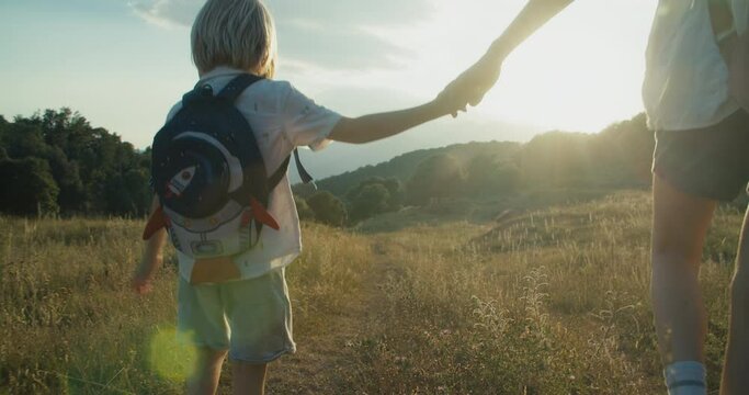 Children with backpack holding woman hand and walk on summer vacation mountain travel. Family explore the world together. Concept of healthy lifestyle and carefree childhood on nature. 