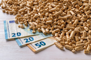 Wood pellets heap and euro money banknotes close-up. Bio fuel costs, buy and sell pellets. Organic biofuel from compressed sawdust prices. Ecological heating, alternative energy concepts.