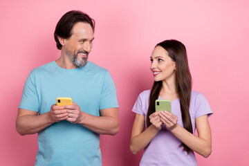 Photo of two positive idyllic people hold telephone look each other isolated on pink color background