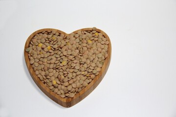 Lentils (Lens culinaris) in a heart-shaped bowl on a white background, top view.