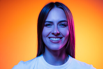 Closeup face of young attractive girl looking at camera isolated on orange color background in neon...