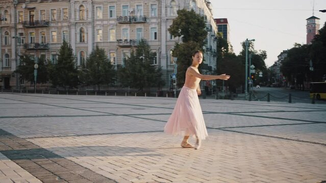 Graceful woman spins on pointe shoes raising hands on square