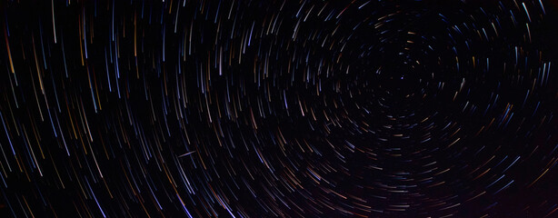 Star trails in the night sky with long exposure. Lines of colored stars. Movement of stars over the Earth. Starry background