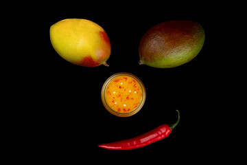 Funny face made of mango, chili and mango chili sauce on black background