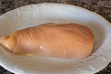 Uncooked chicken breast on a white plate.