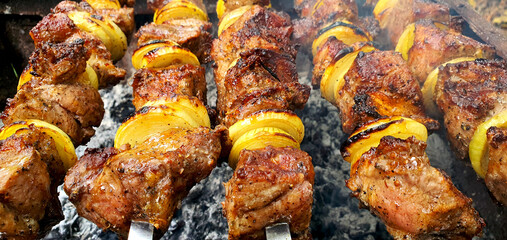 Pieces of pork with onions on skewers are fried on the grill close-up. Traditional kebabs that are cooked for the holidays in Ukraine. The meat is well cooked and ready to eat
