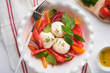 Caprese salad. Italian caprese salad with sliced tomatoes, mozzarella cheese, basil, olive oil in white plate over white background. Delicious Italian food. Top view. Rustic style.