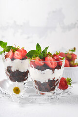 Trifles. Brownies, fresh strawberry and mascarpone cream servered in layers on glass on white background. Portion desserts. No baked brownie cheesecake with fresh berries in a glass.