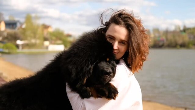 Smiling woman hugging tibetan mastiff dog looking at camera outdoors. Girl and dog playing on the beach