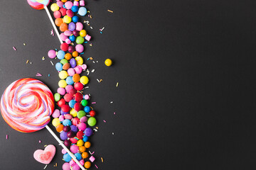 Overhead view of lollipops with colorful candies and sprinklers by copy space on black background