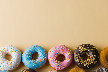 Directly above view of fresh donuts with sprinklers arranged by copy space on beige background - Powered by Adobe