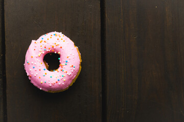 Directly above view of fresh pink donut with sprinklers on wooden table