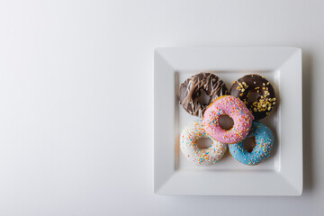 Directly above view of fresh multi colored donuts in square plate by copy space on white background © wavebreak3