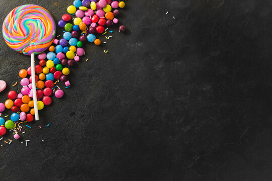 Directly above view of swirl lollipop with multi colored chocolate candies on black table