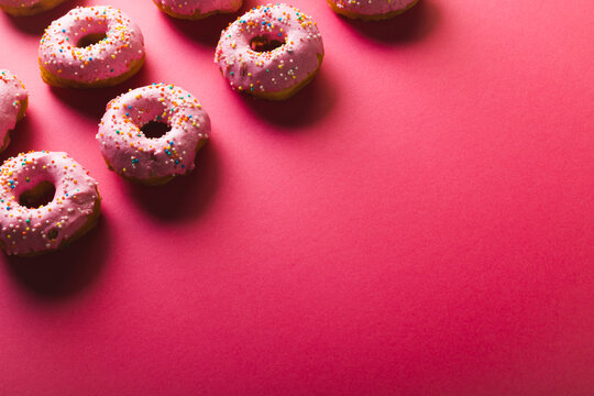 High angle view of copy space by arranged donuts with sprinklers on pink background