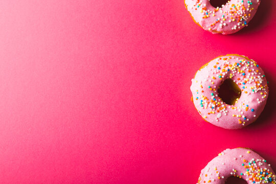 Directly above view of pink donuts with sprinklers arranged by copy space on colored background