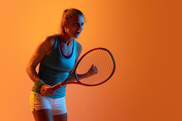 Portrait of motivated woman, professional tennis player training isolated over orange studio background in neon light