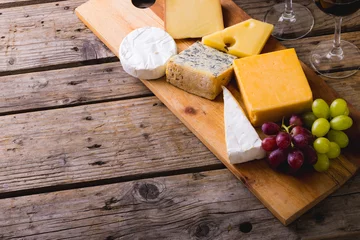 Tuinposter High angle view of various cheese with grapes on wooden board at table, copy space © WavebreakMediaMicro