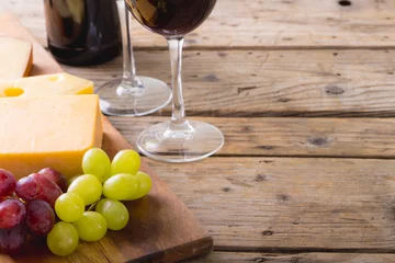 Foto auf Glas Close-up of cheese with grapes on wooden board by wineglasses on table, copy space © WavebreakMediaMicro