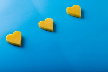 Tuinposter High angle view of heart shaped yellow cheese arranged on blue background, copy space © wavebreak3
