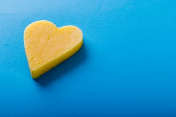 Plexiglas foto achterwand High angle view of heart shaped yellow cheese on blue background, copy space © WavebreakMediaMicro
