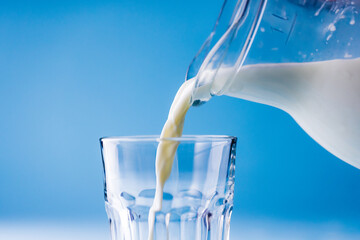 Close-up of milk being poured in glass from jar against blue background, copy space