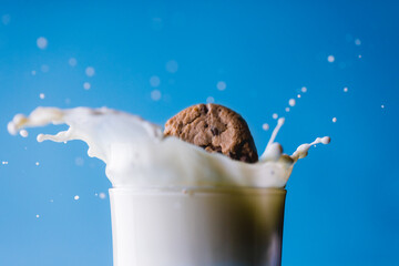 Close-up of spilled milk with cookie in glass against blue background, copy space